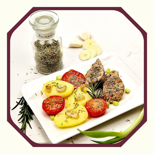 Rosmarin im Glas neben einem Teller mit Kartoffeln, Tomaten und Schweinefilet in Rosmarin-Wein-Sauce