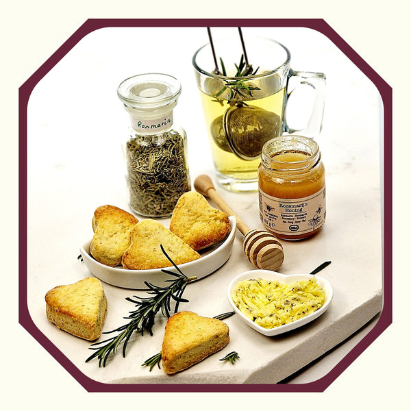 Rosmarin im Glas neben Rosmarin-Scones in Herzform, kleine Schale mit Thymian-Butter, ein Glas Rosmarin-Honig, ein Teeglas Rosmarin-Tee