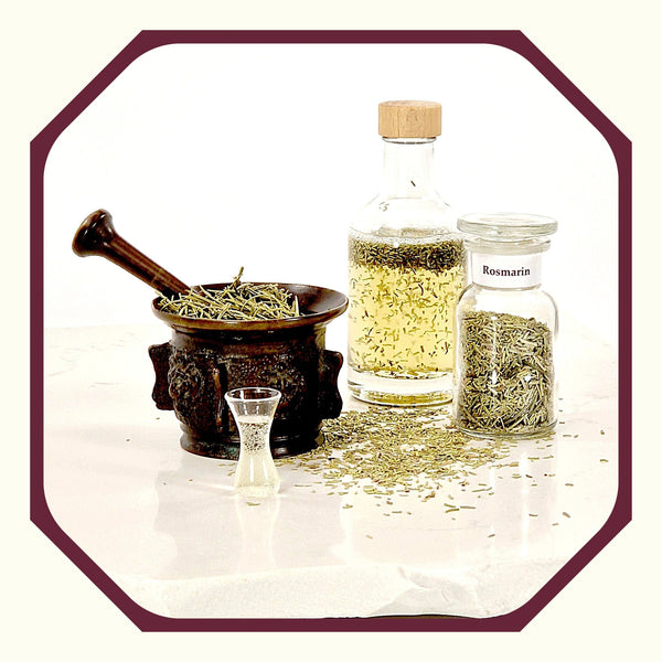 Rosmarin im Glas neben einem antiken Mörser, gefüllt mit Rosmarin, einer Flasche mit Rosmarin-Wein und einem kleinen Glas für Aperitif