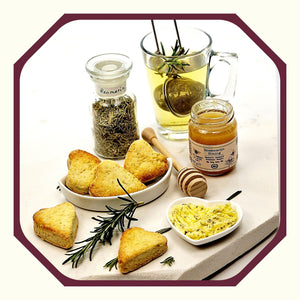 Rosmarin im Glas neben Rosmarin-Scones in Herzform, kleine Schale mit Thymian-Butter, ein Glas Rosmarin-Honig, ein Teeglas Rosmarin-Tee
