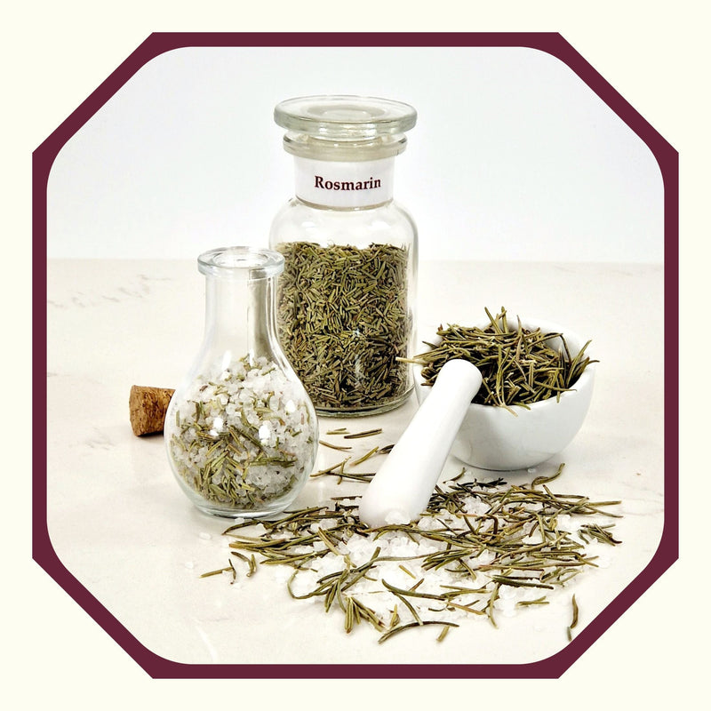 Rosmarin im Glas neben einem Glas mit Rosmarin-Peeling-Salz, einem kleinen weißen Mörser mit Rosmarinnadeln und Rosmarin und Salz