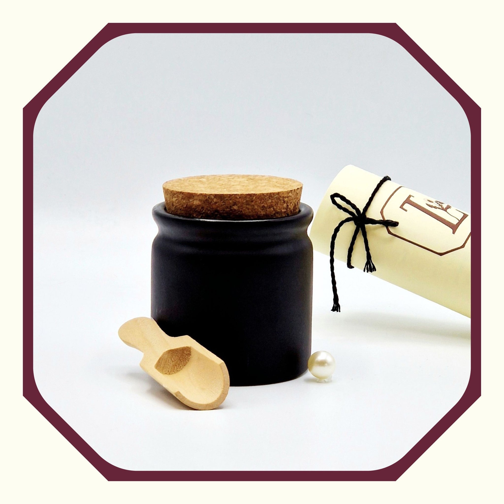 Eine Perle, eine rund gefaltete Karte mit schwarzem Schleifenband, ein Salz-Topf aus Keramik mit Korkendeckel, eine kleine Salzschaufel aus Holz