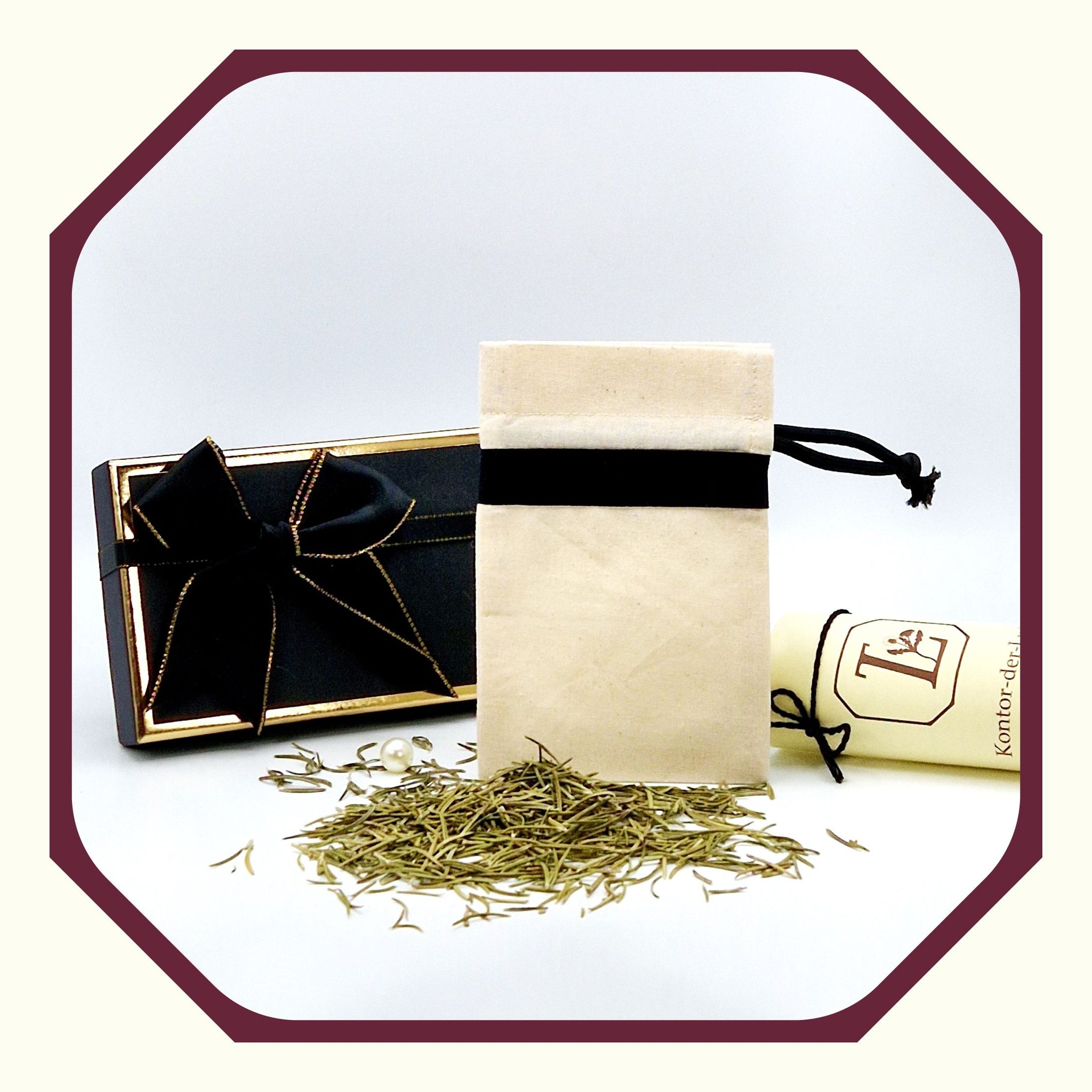 Eine Perle, eine rund gefaltete Karte mit schwarzem Schleifenband, ein Kräuter Säckchen aus Leinen vor einer kleinen Luxus  Geschenkbox, davor Rosmarin