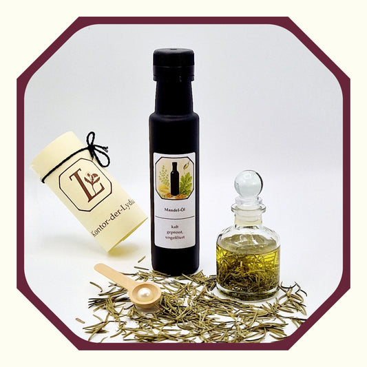 Eine Perle, eine rund gefaltete Karte mit schwarzen Schleifenband, eine Flasche Mandel-Öl, davor eine Glasflasche mit selbst hergestellten Mandelöl, daneben Rosmarin, Kräuter-Löffel aus Holz